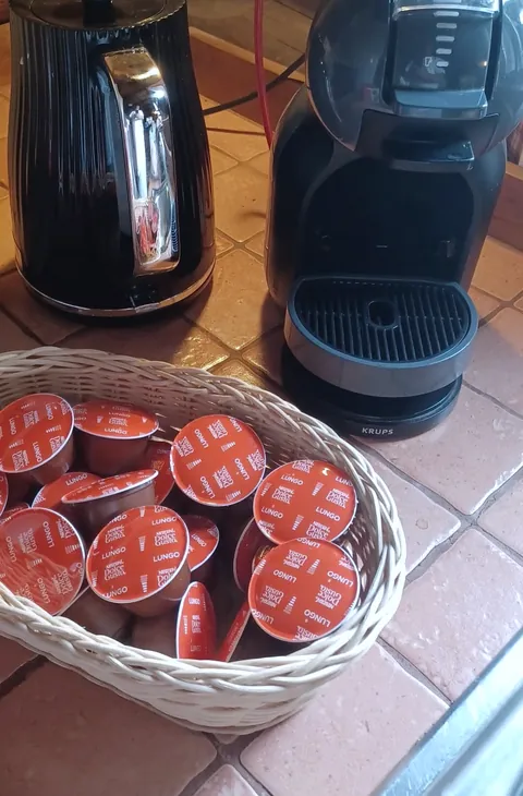 Kávovar Dolce Gusto, čierna kanvica a košík s kapsulami.