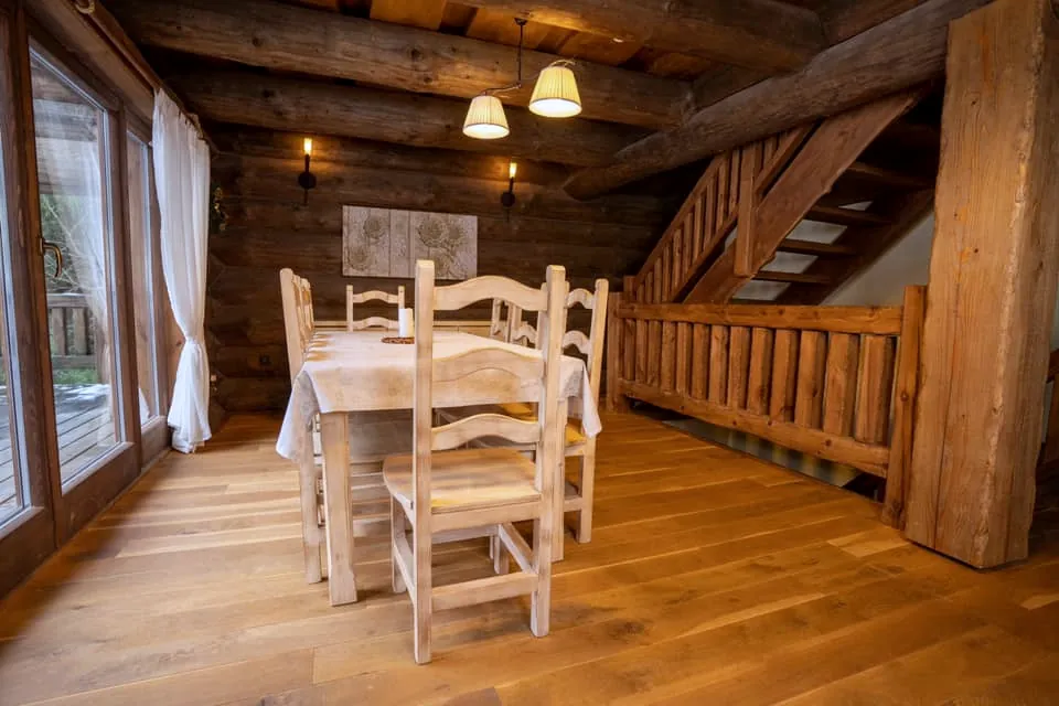 Jedálenský stôl pri francúzskych oknách, za ním schody hore so zábradlím z guľatiny.