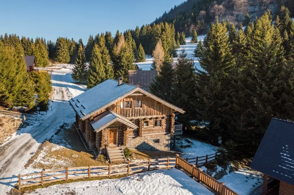 Trojpodlažný zrub z guľatiny v zime zhora, k domu vedie zasnežená cesta, vpravo tmavé smreky.